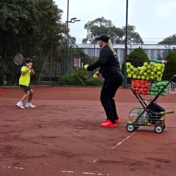 Slamin Tennis coach running a drill with a junior player on a clay court
