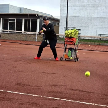 Slamin Tennis coach feeding balls from the ball cart on a clay court