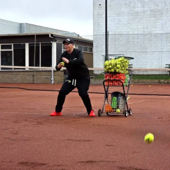 Slamin Tennis coach feeding balls from the ball cart on a clay court
