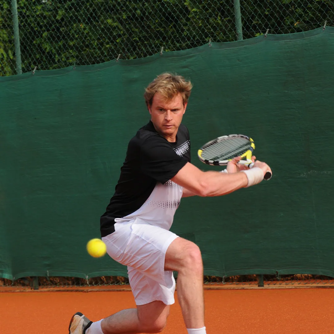 Man bending low for a volley on a clay court