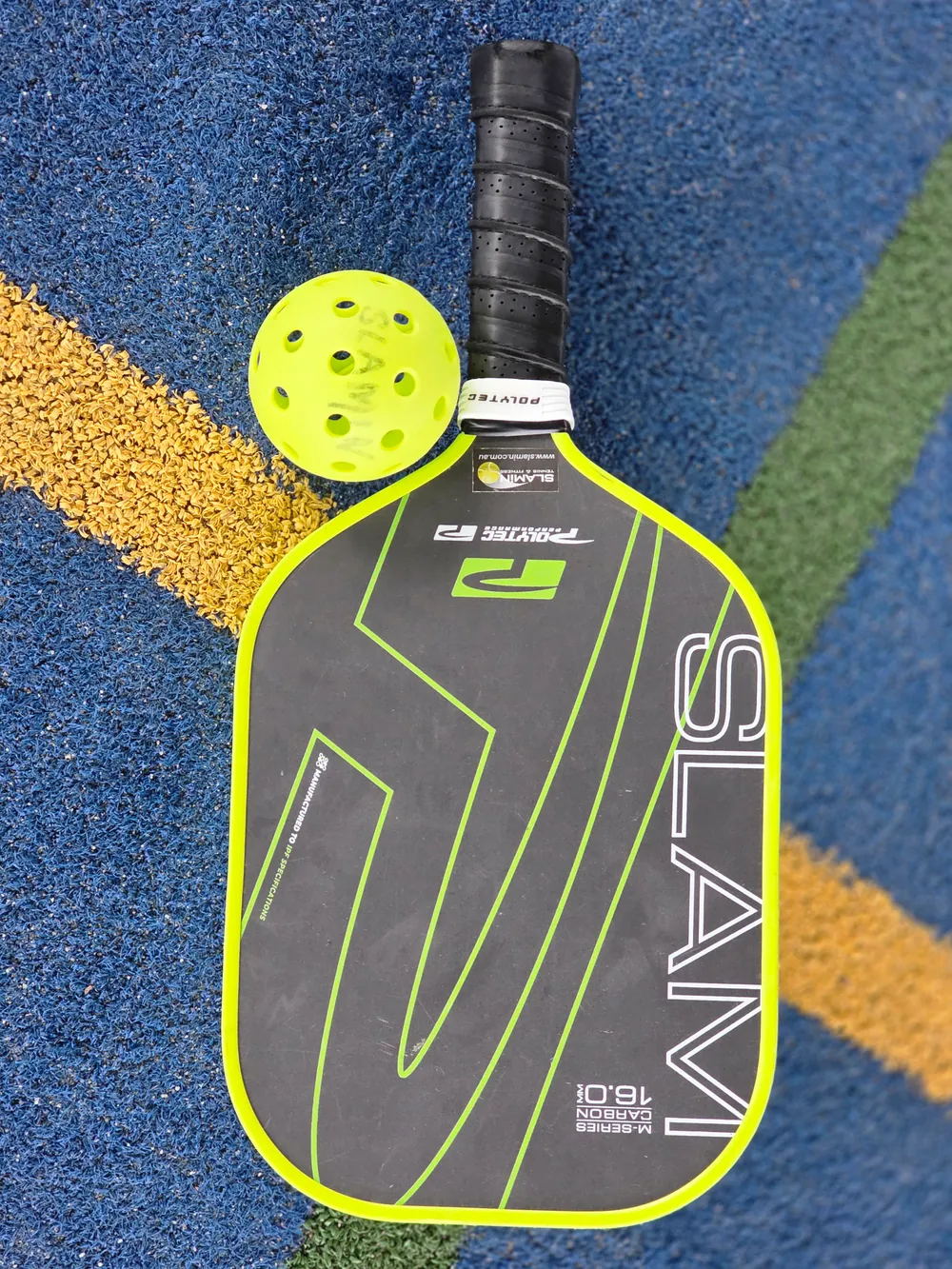 Pickleball paddle and ball resting on a blue court