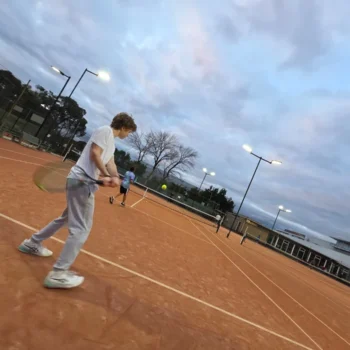 Player preparing a backhand during an evening session on a clay court