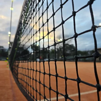 Close-up of a tennis net on a clay court at dusk